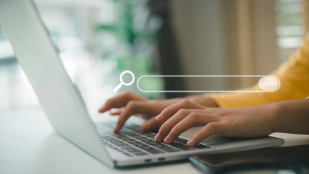 Typing in search bar on laptop, illustrating search engine optimization process.