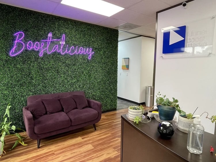 Funnel Boost Media's front office featuring a green wall with the word 'Boostalicous,' a couch, and the company logo displayed on signage.