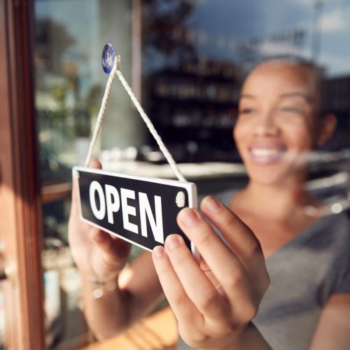 woman in storefront flipping open sign on door